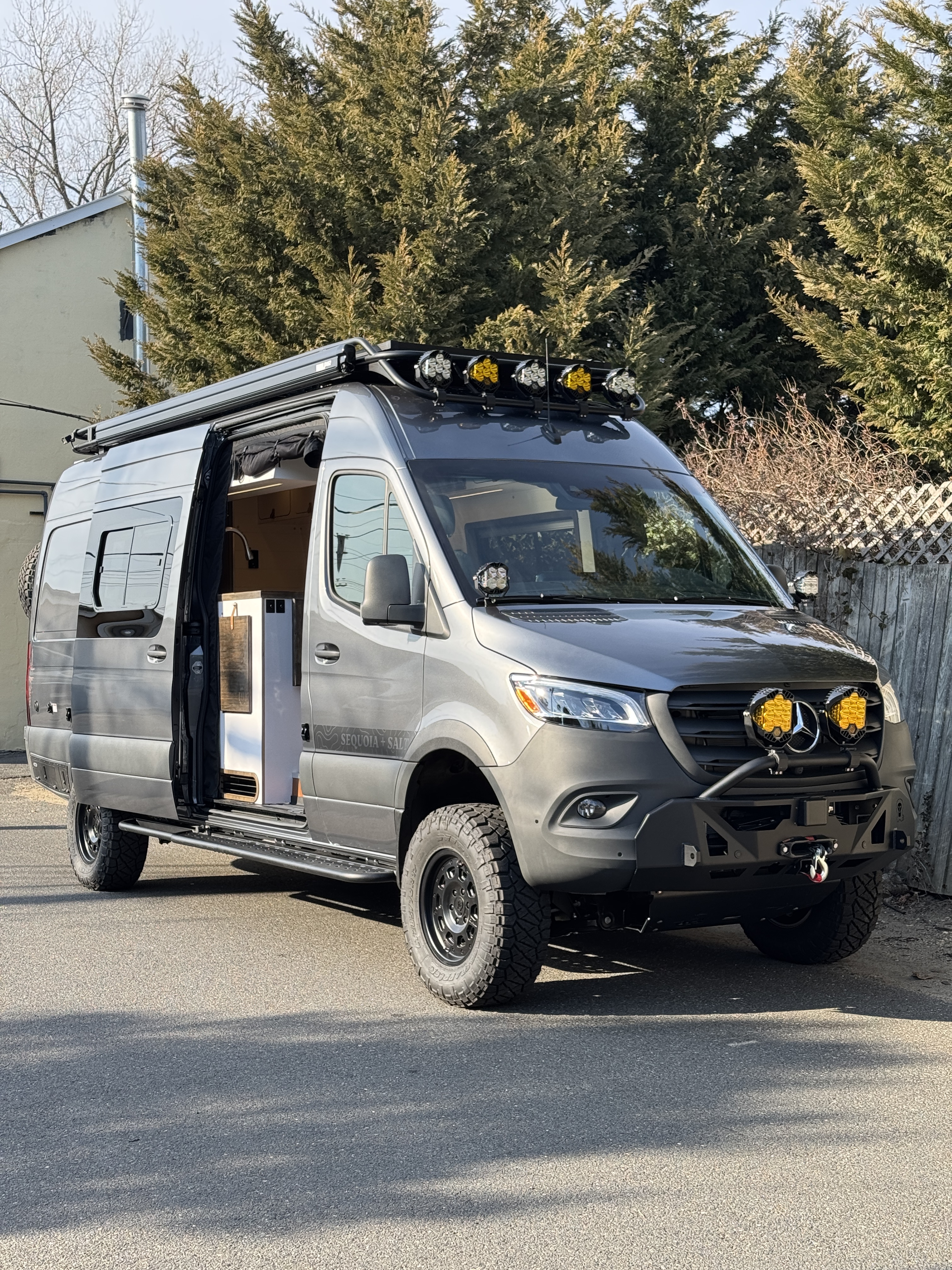Baja Sprinter 170 4x4 — passenger-side slider door open at the shop showing galley interior, full off-road kit, and rear bathroom