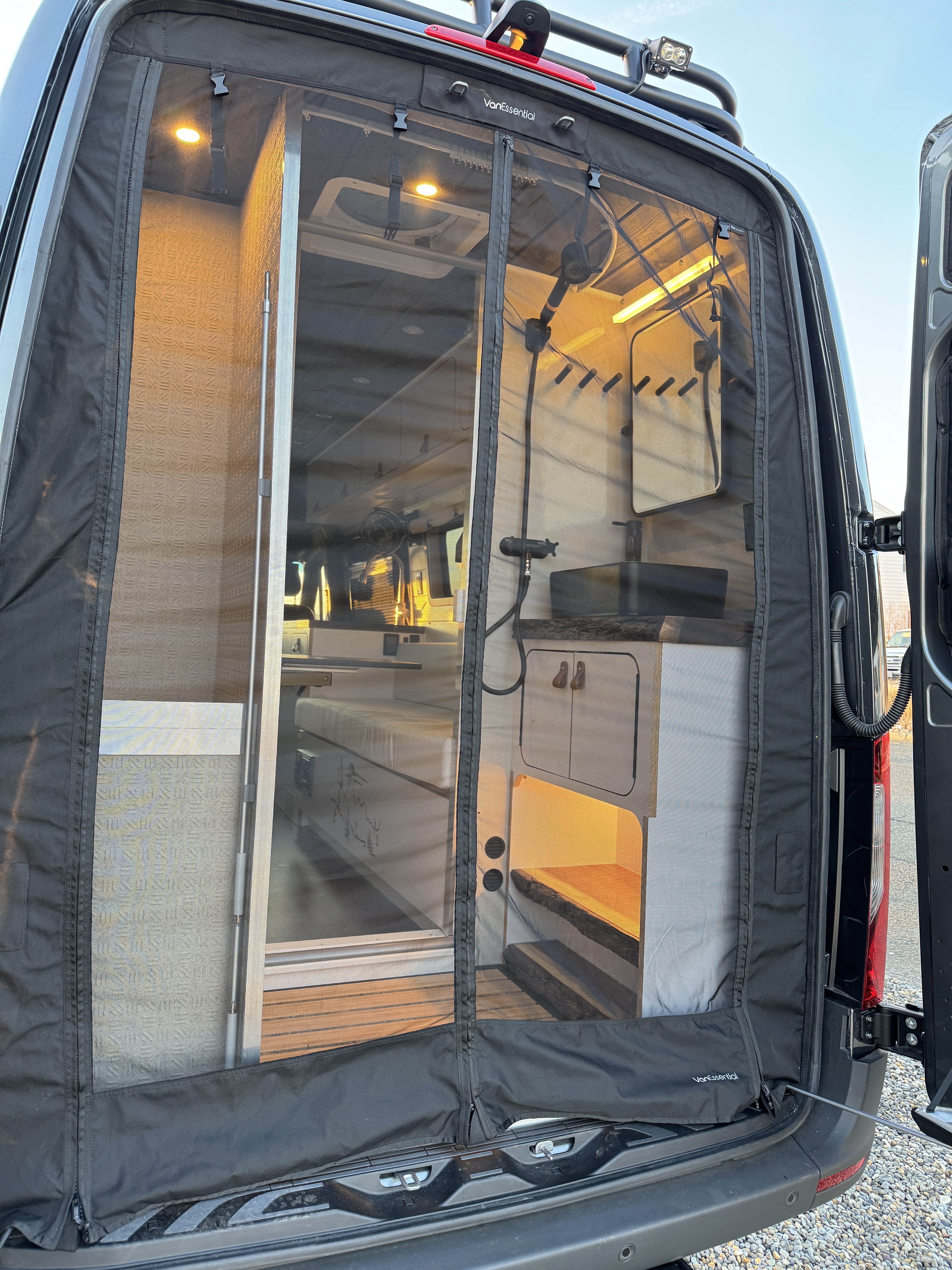 Baja Sprinter 170 4x4 — VanEssential bug screen closed at dusk with warm interior light glowing through