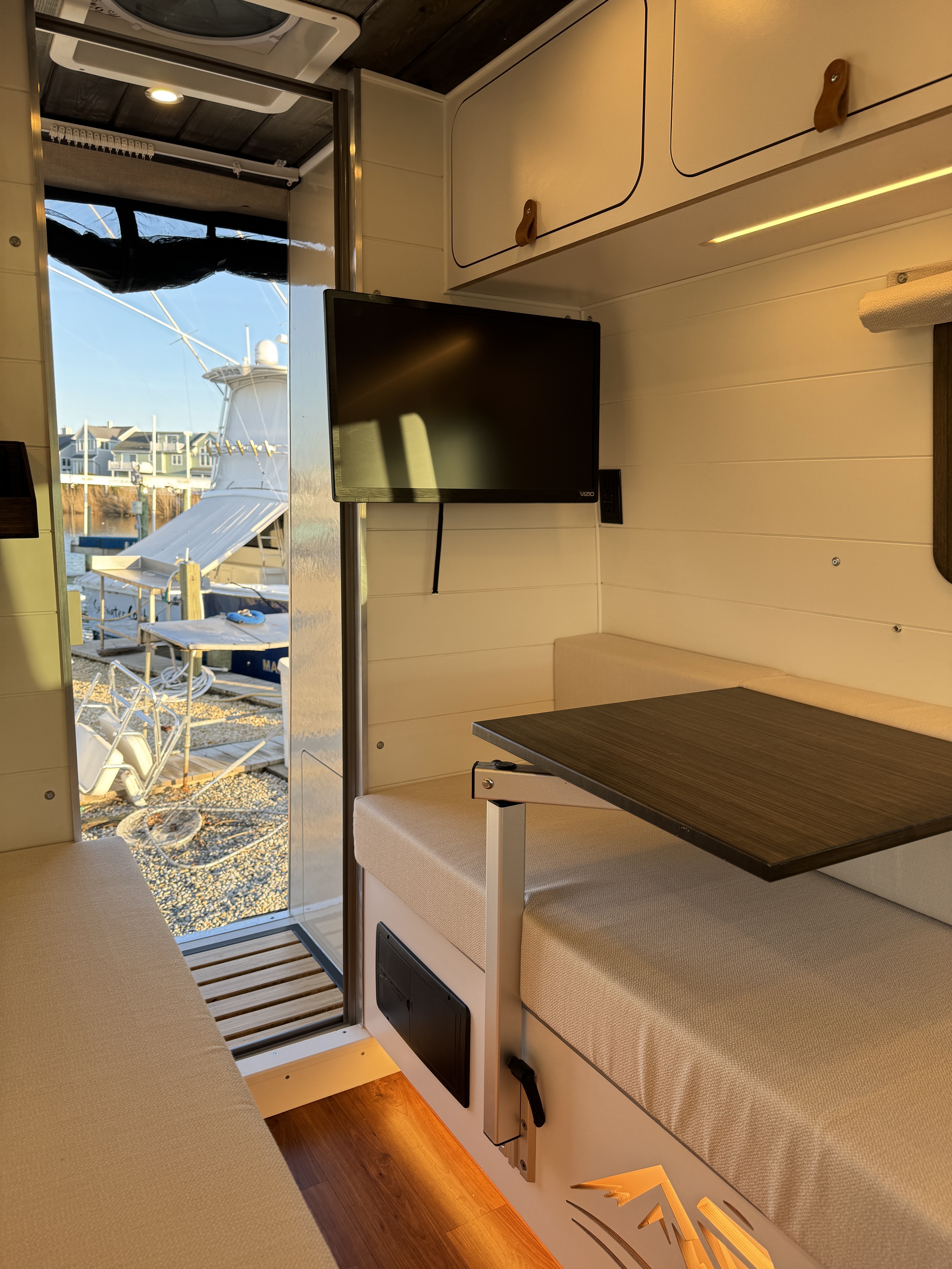 Baja Sprinter 170 4x4 — interior dinette with mounted TV at golden hour and slider door open to marina