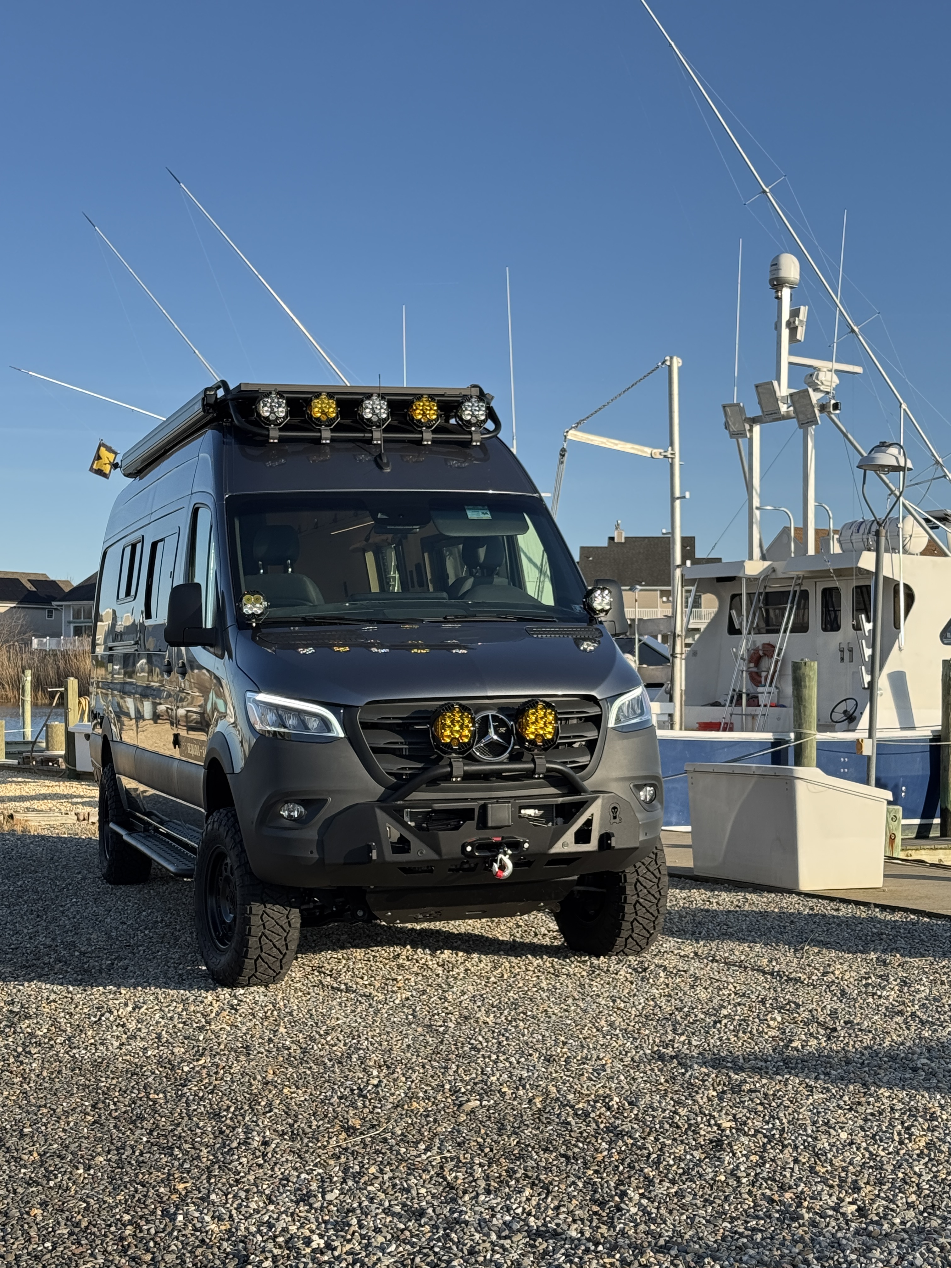 Baja Sprinter 170 4x4 — front three-quarter exterior at the marina with Baja Designs LP9 light bar, winch bumper, and 35-inch off-road tires, full vertical profile