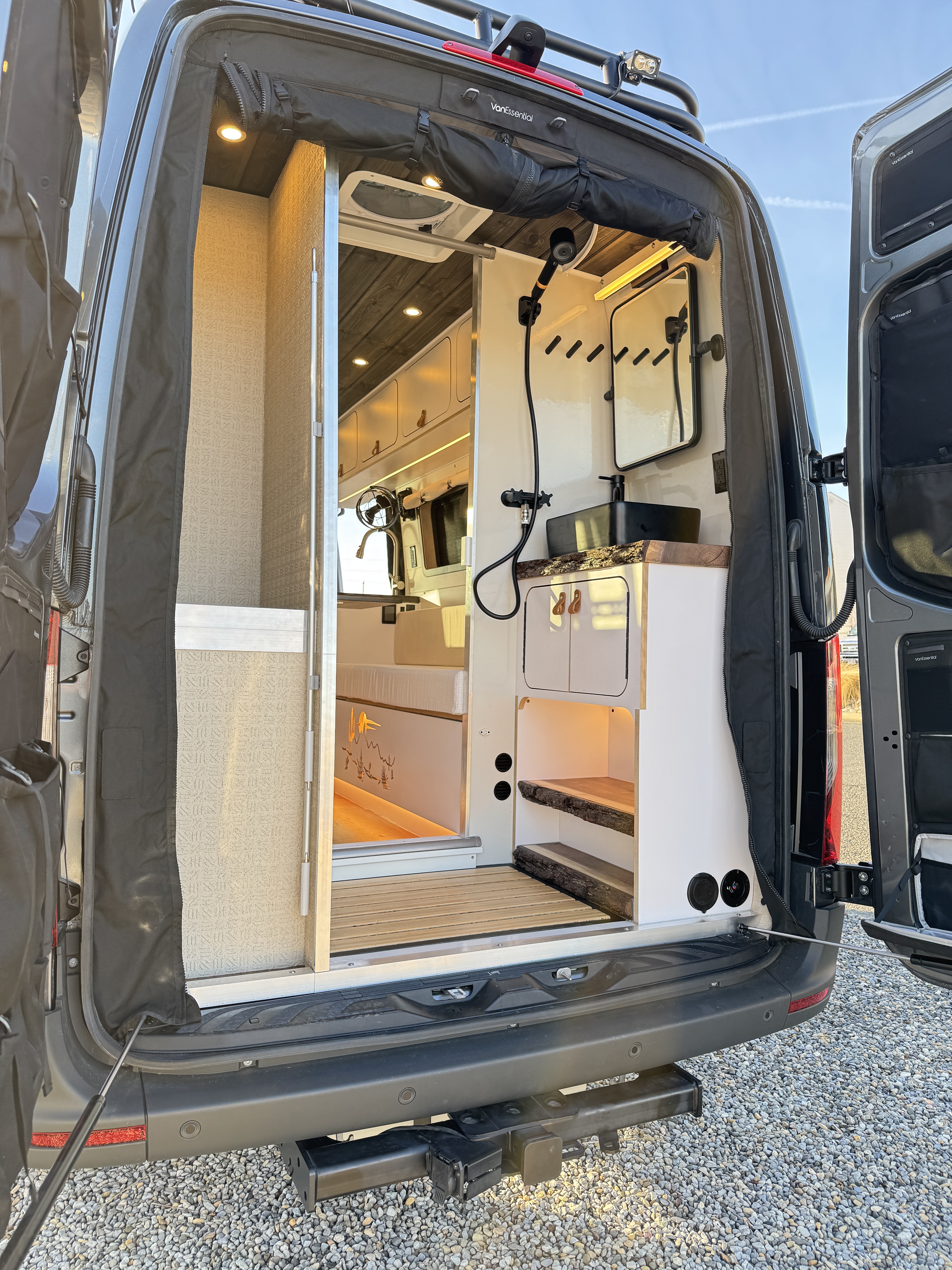 Baja Sprinter 170 4x4 — rear doors open showing wet bath with live-edge wood counter, vessel sink, shower system, and view through to main cabin