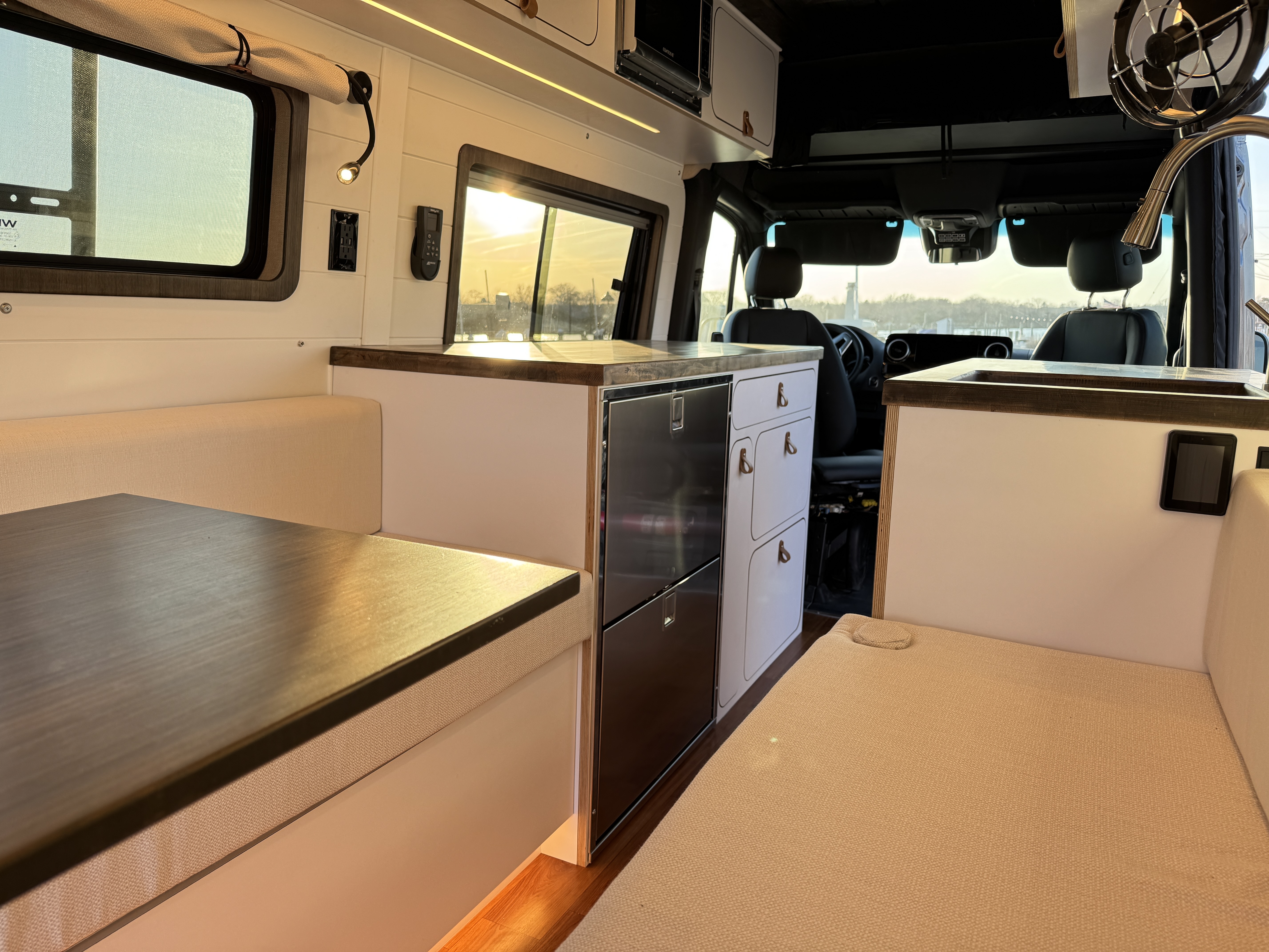 Baja Sprinter 170 4x4 — interior at golden hour from rear lounge looking forward through galley with butcher block counter, Isotherm drawer fridge, and U-shaped seating