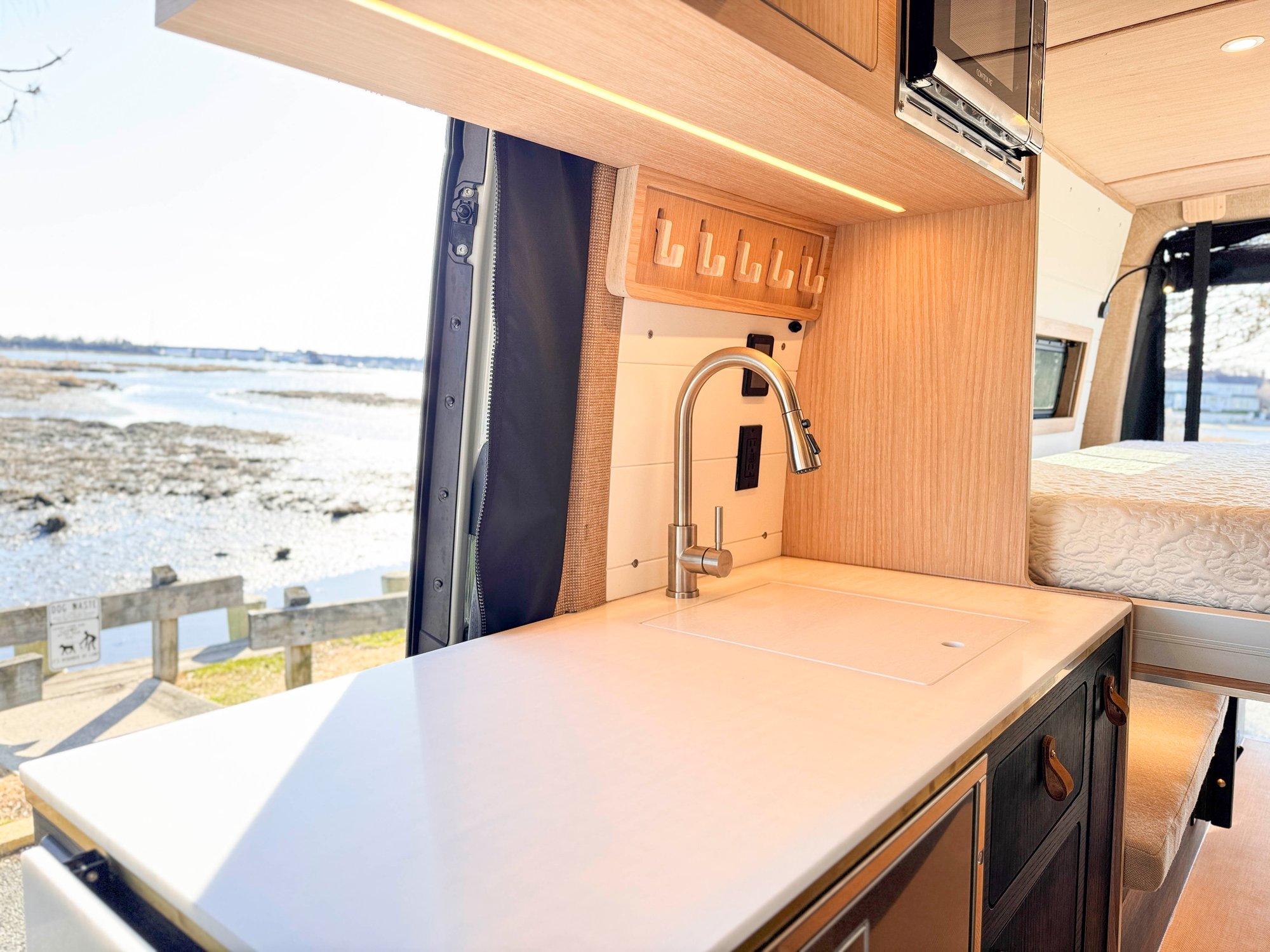 The Loft galley from the side — sink, faucet, microwave and fridge, bed and marina beyond