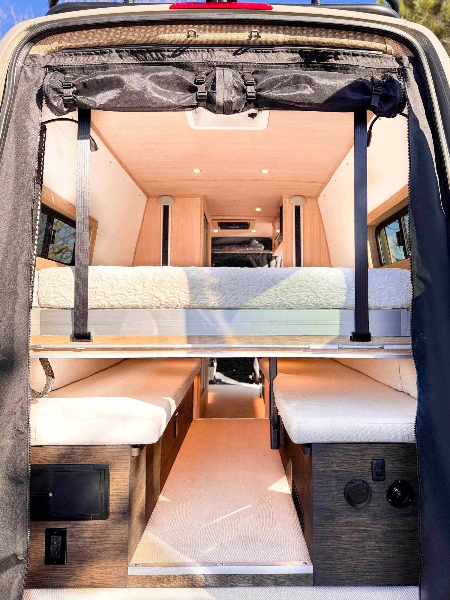 The Loft — north-south lift bed raised above the lounge, walk-up aisle down the center, seen through the open rear doors