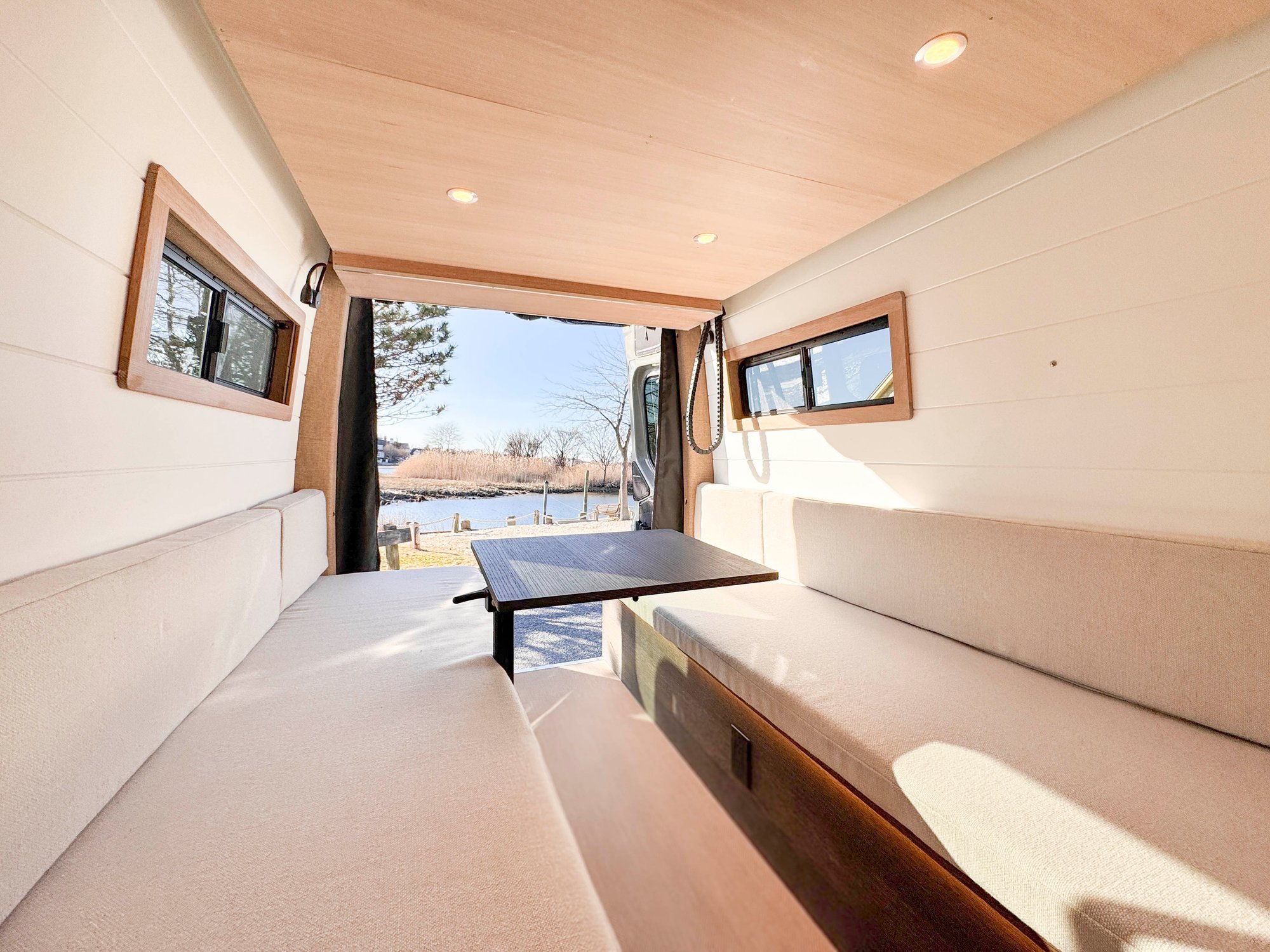 The Loft convertible north-south lounge in day mode — facing oatmeal benches and a deployed table, marina view through the open rear doors