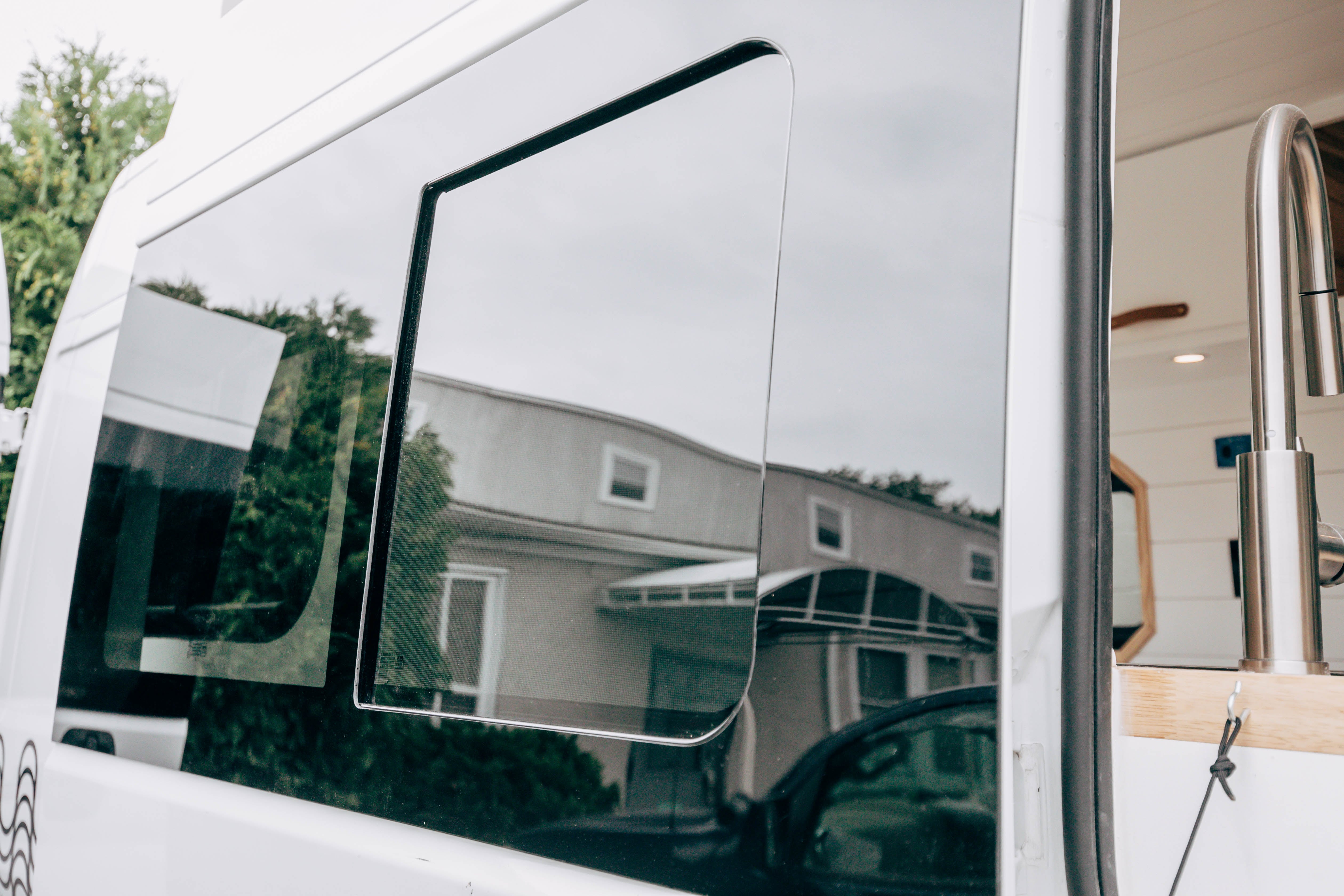 Riverside ProMaster 159 campervan side window with a house reflected in the glass