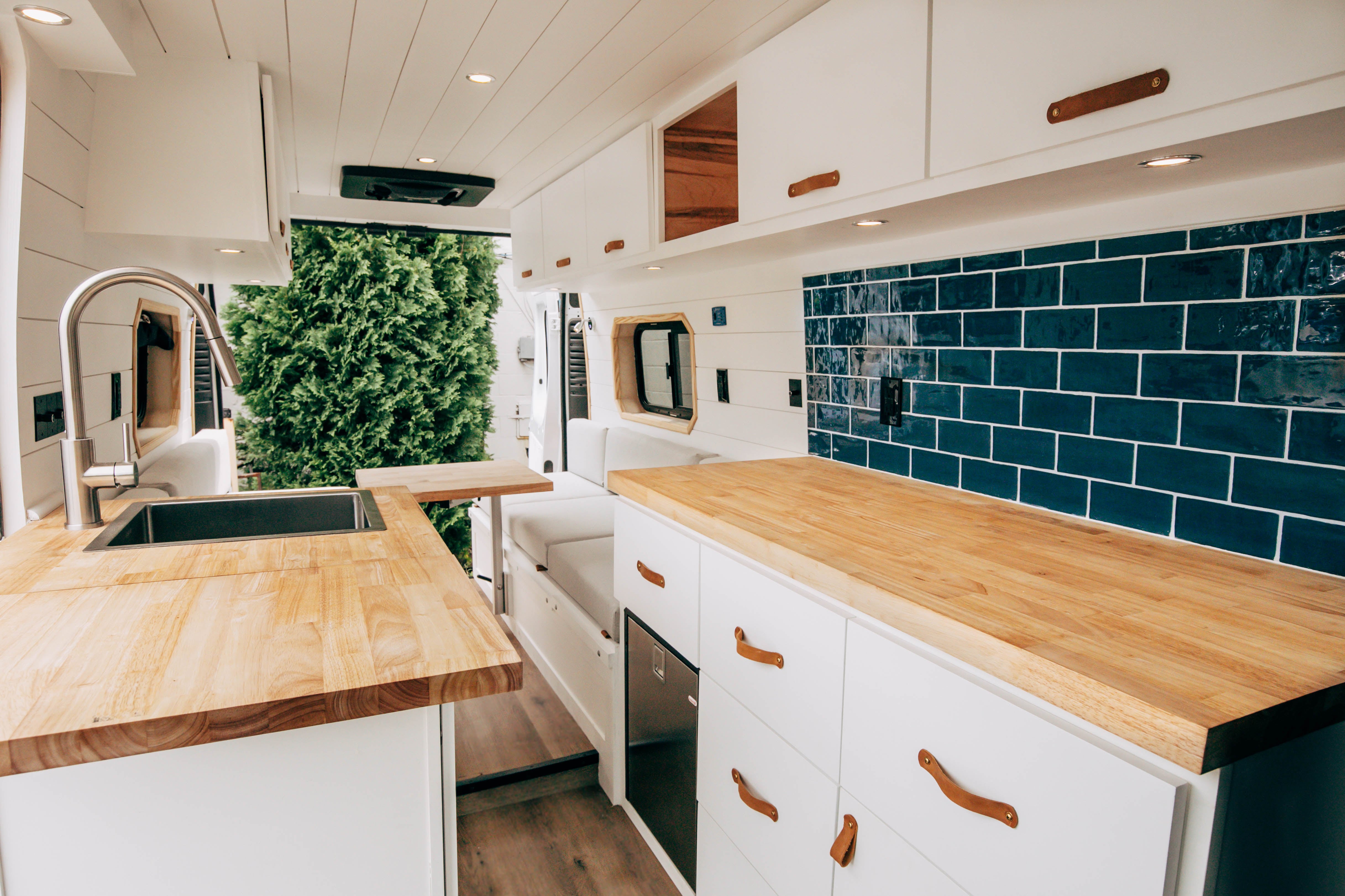 Riverside ProMaster 159 campervan galley with butcher-block counter and navy subway-tile backsplash