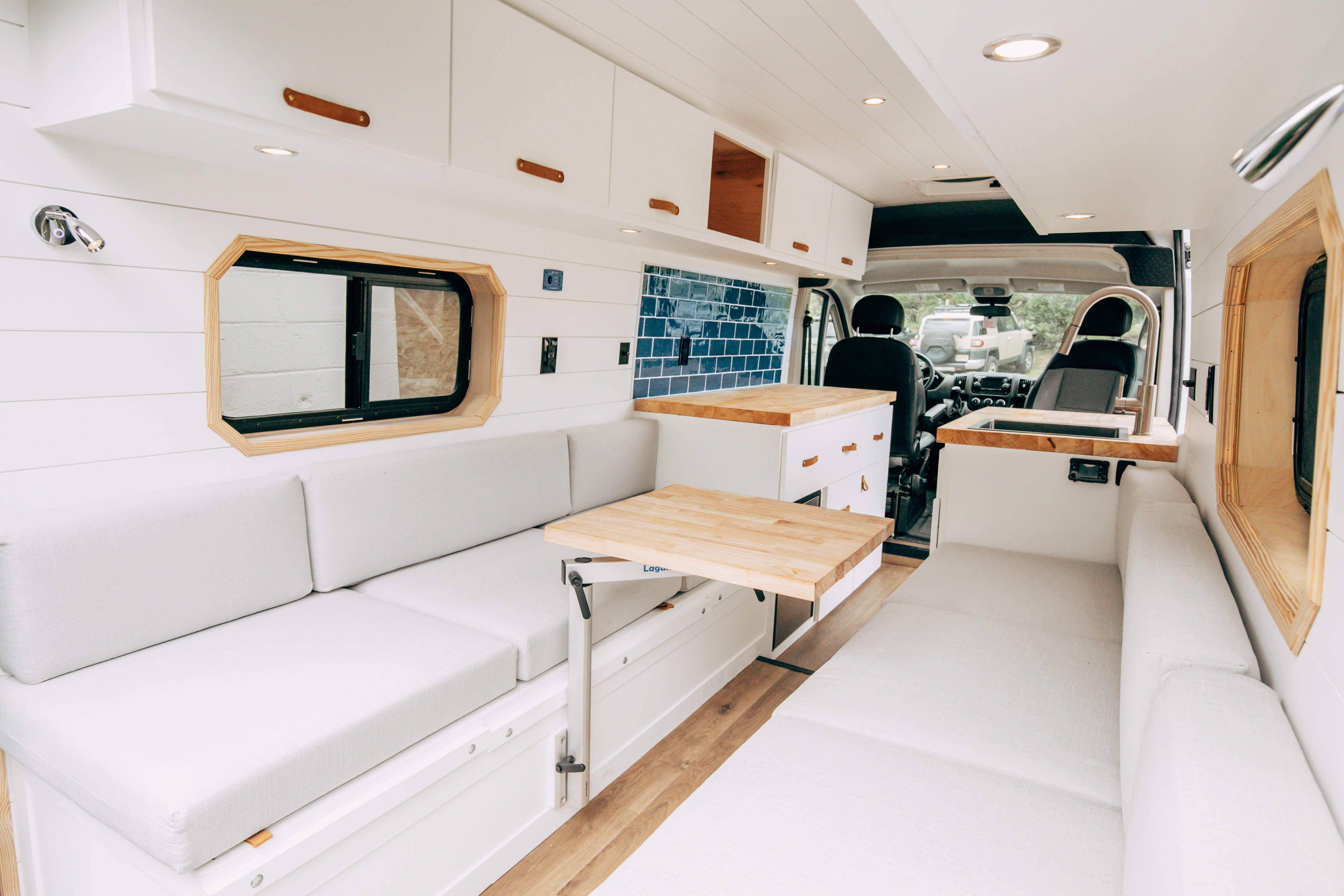 Riverside ProMaster 159 campervan lounge with white benches and a deployed wood table