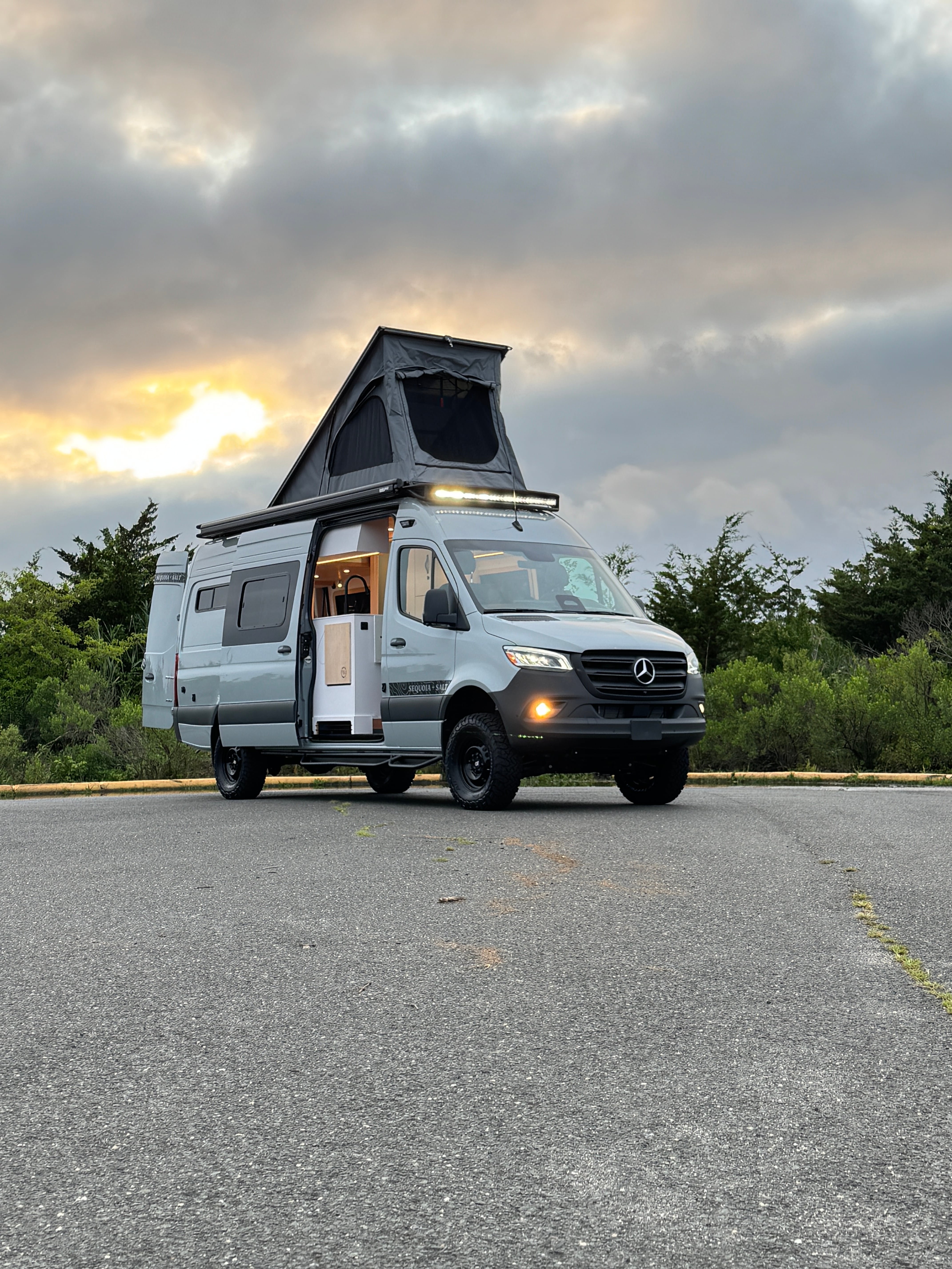 Skyrise Sprinter 170 campervan at dusk with the pop-top up and warm interior light