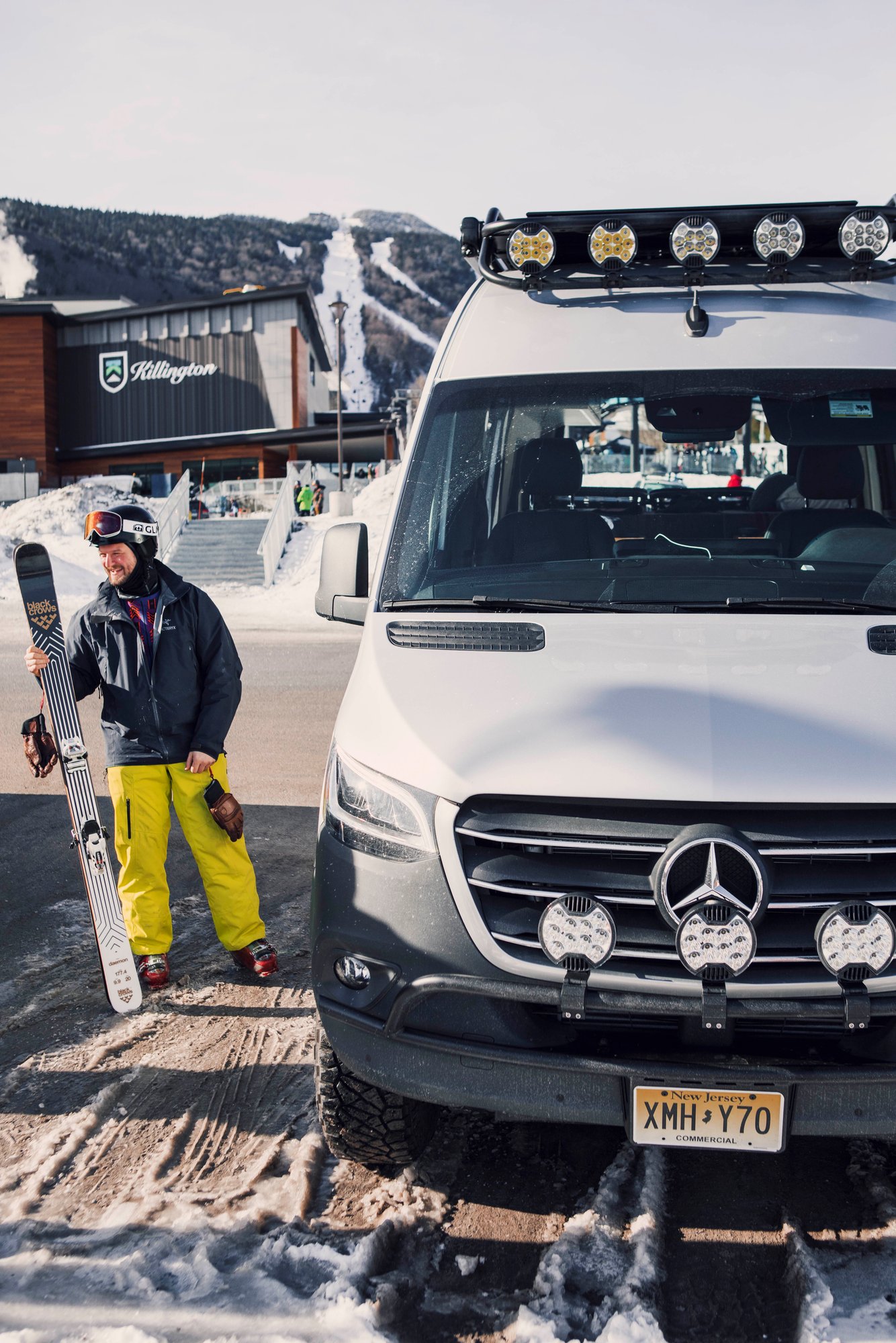 A Stoke owner with skis beside the Sprinter 144 at a ski resort