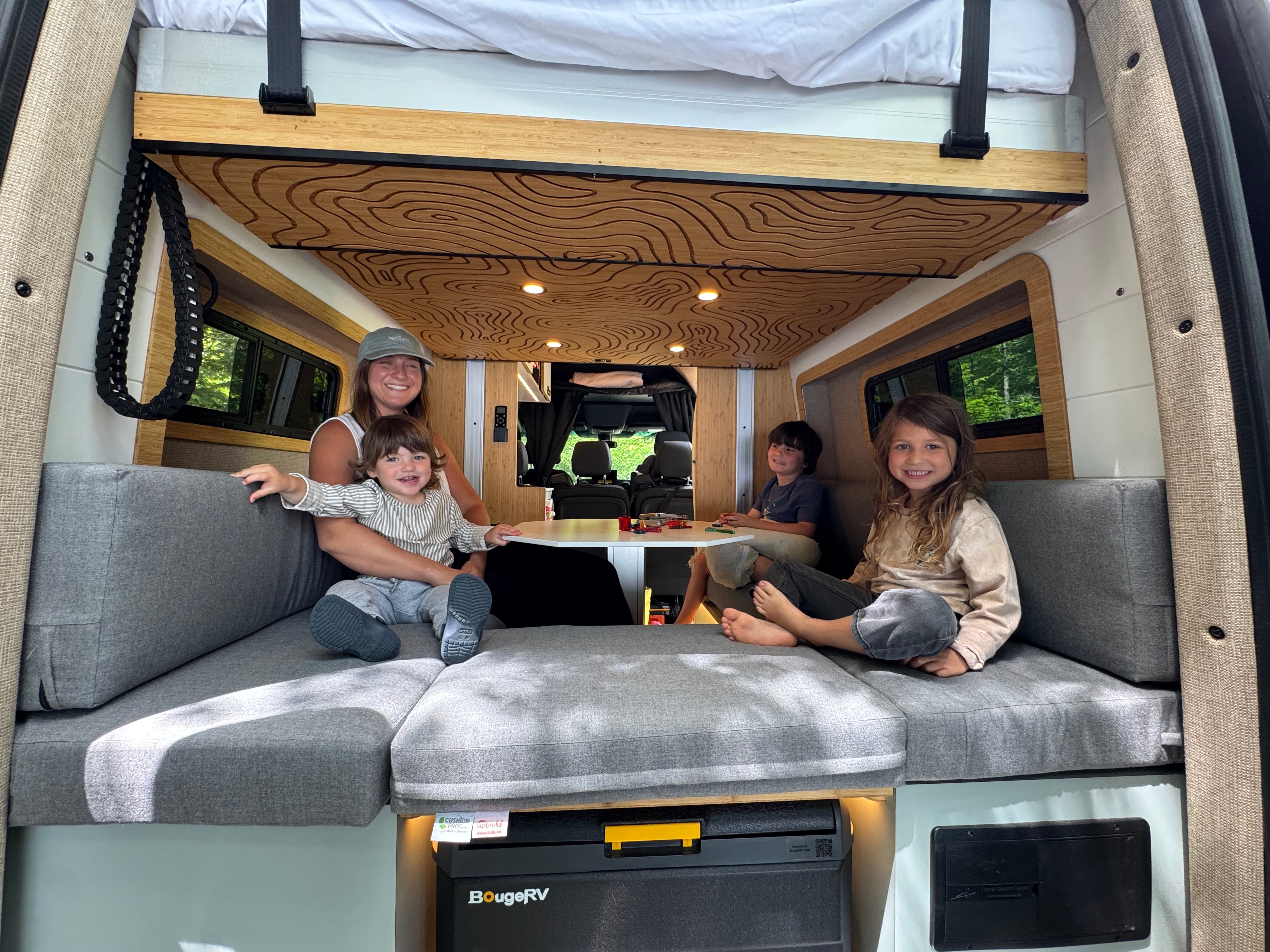The Don Sprinter 144 campervan rear lounge converted to a bed with gray cushions and a wood ceiling