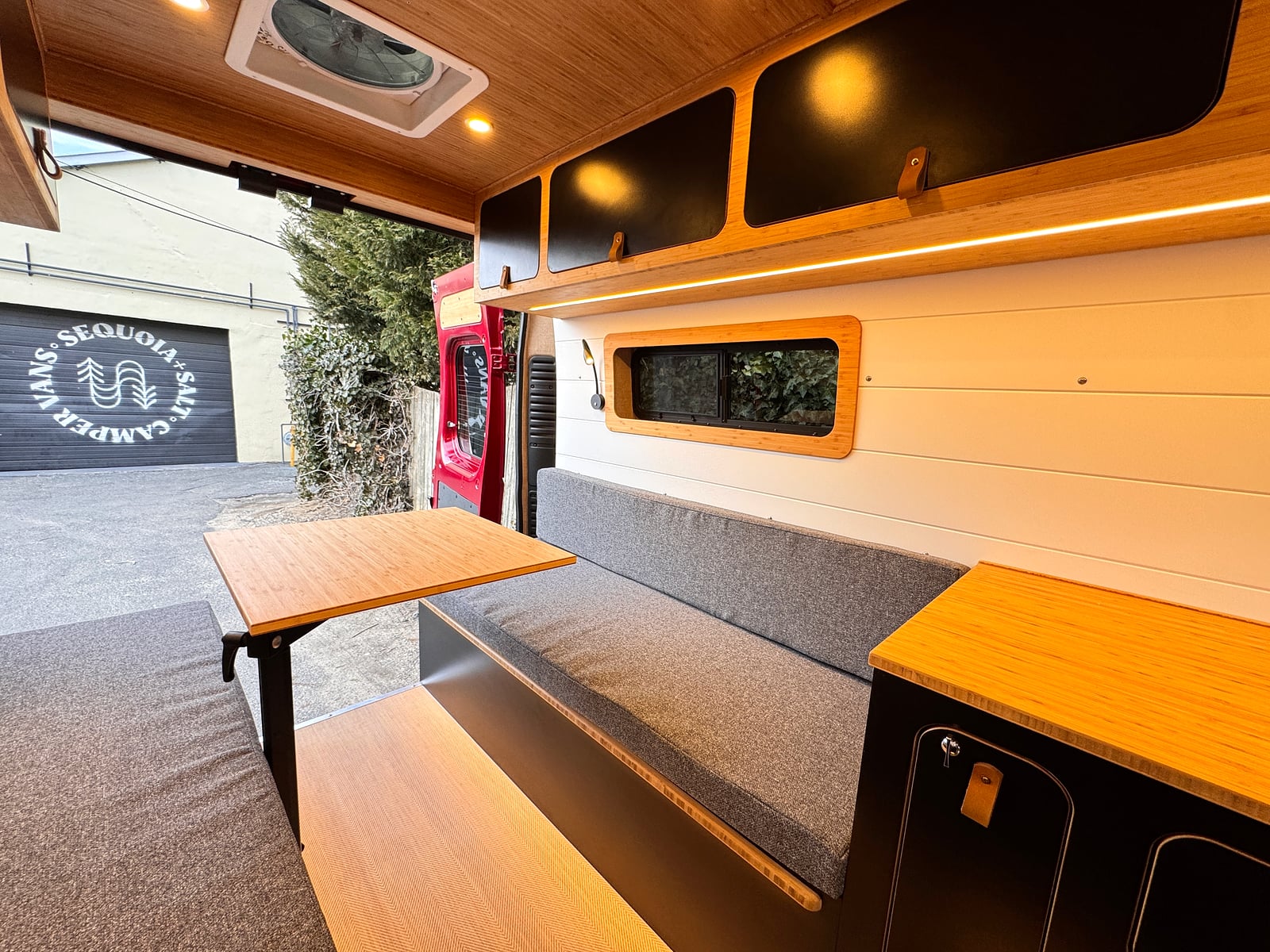 Bobal Mobile Salon — rear lounge with upholstered bench seating and fold-out bamboo table, day mode