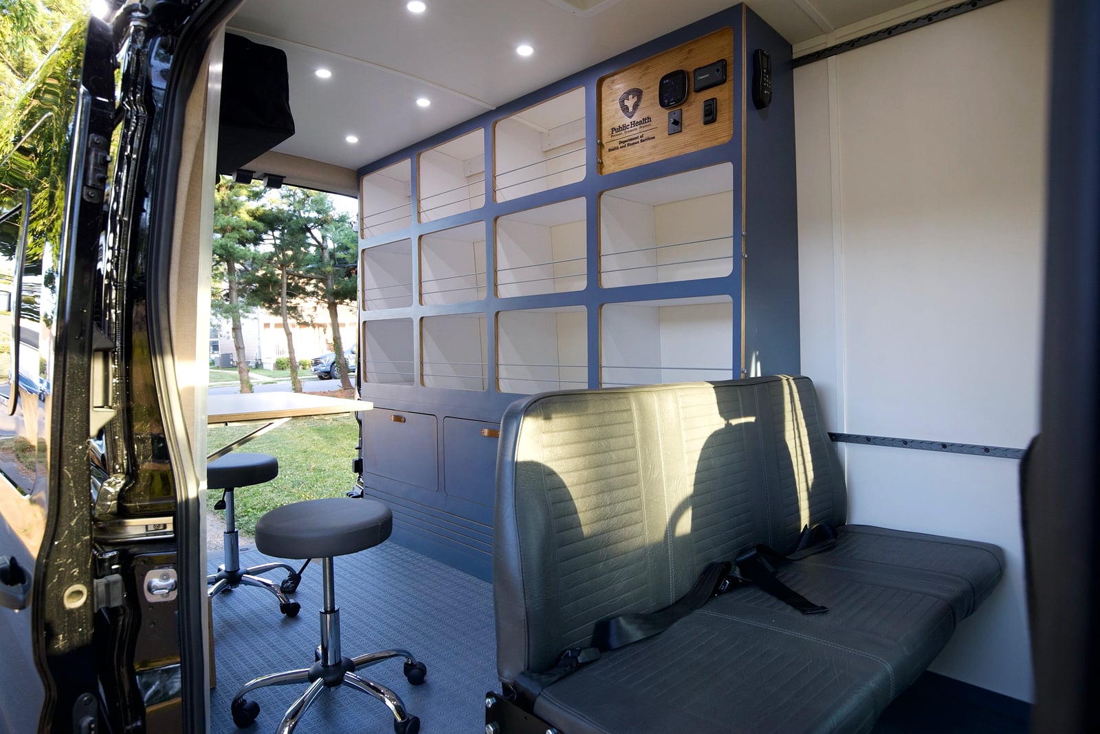 Northampton DCC electric Transit fleet — interior with modular storage wall, bench seating, rolling stool, and a Public Health branded control panel