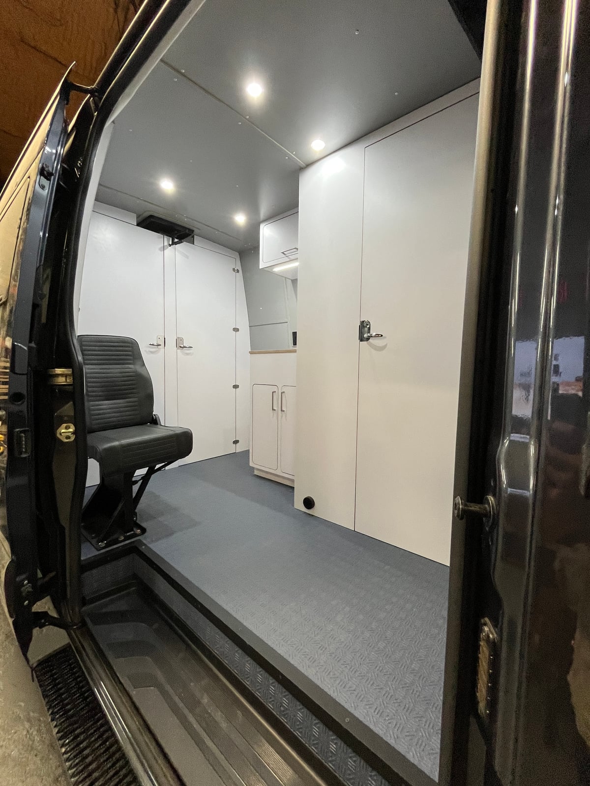 PROCEED Mobile Testing Van — clinical white-panel Sprinter interior with swivel seating and floor-to-ceiling cabinetry, doors open