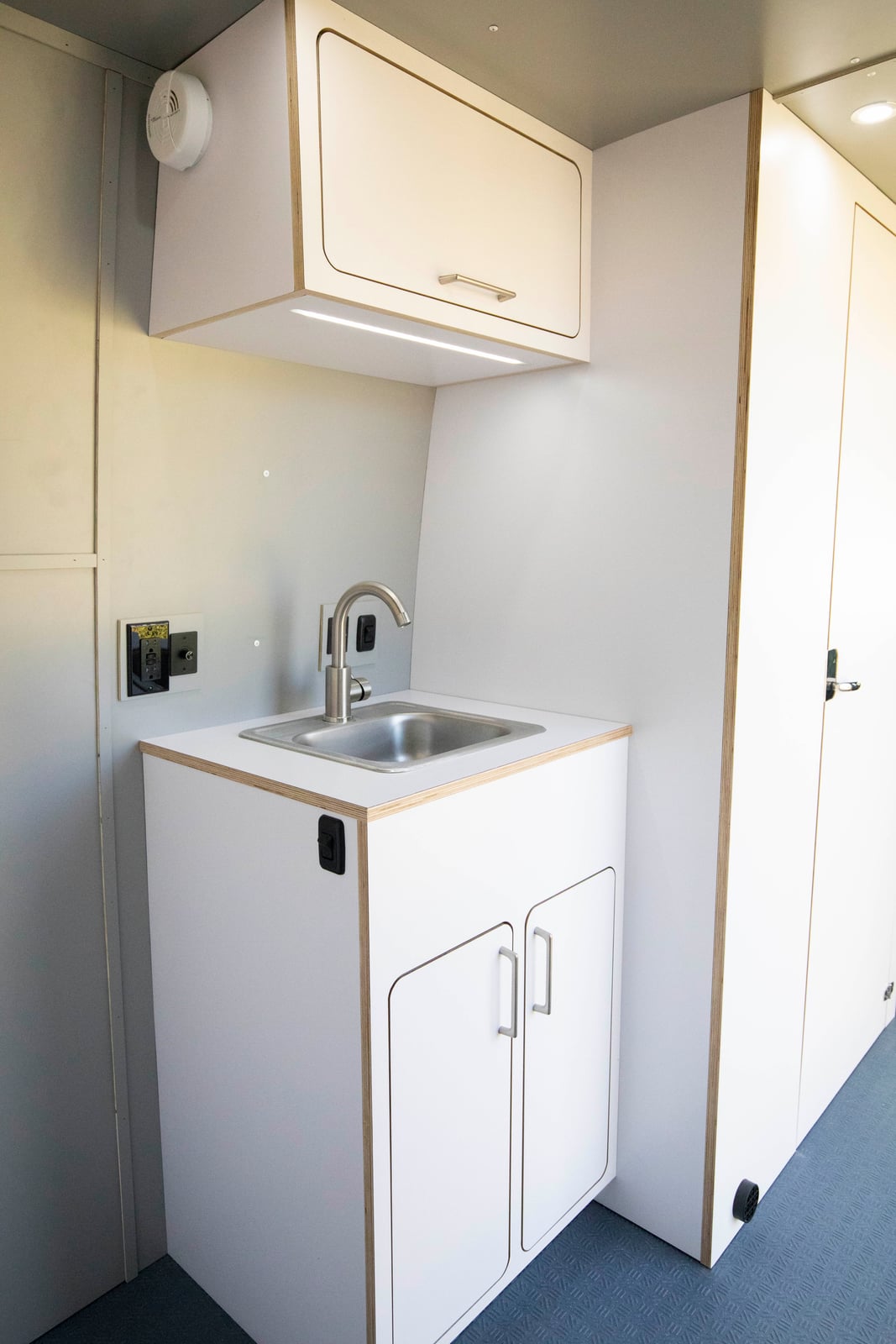 Sprinter mobile testing van — stainless hand-washing sink with baltic-birch cabinetry and under-cabinet lighting