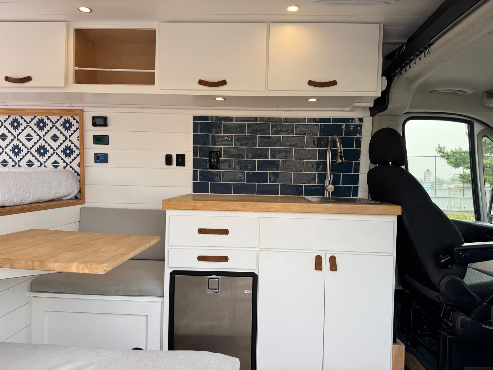 Wide view of the galley and dinette table with the marine refrigerator and navy tile backsplash