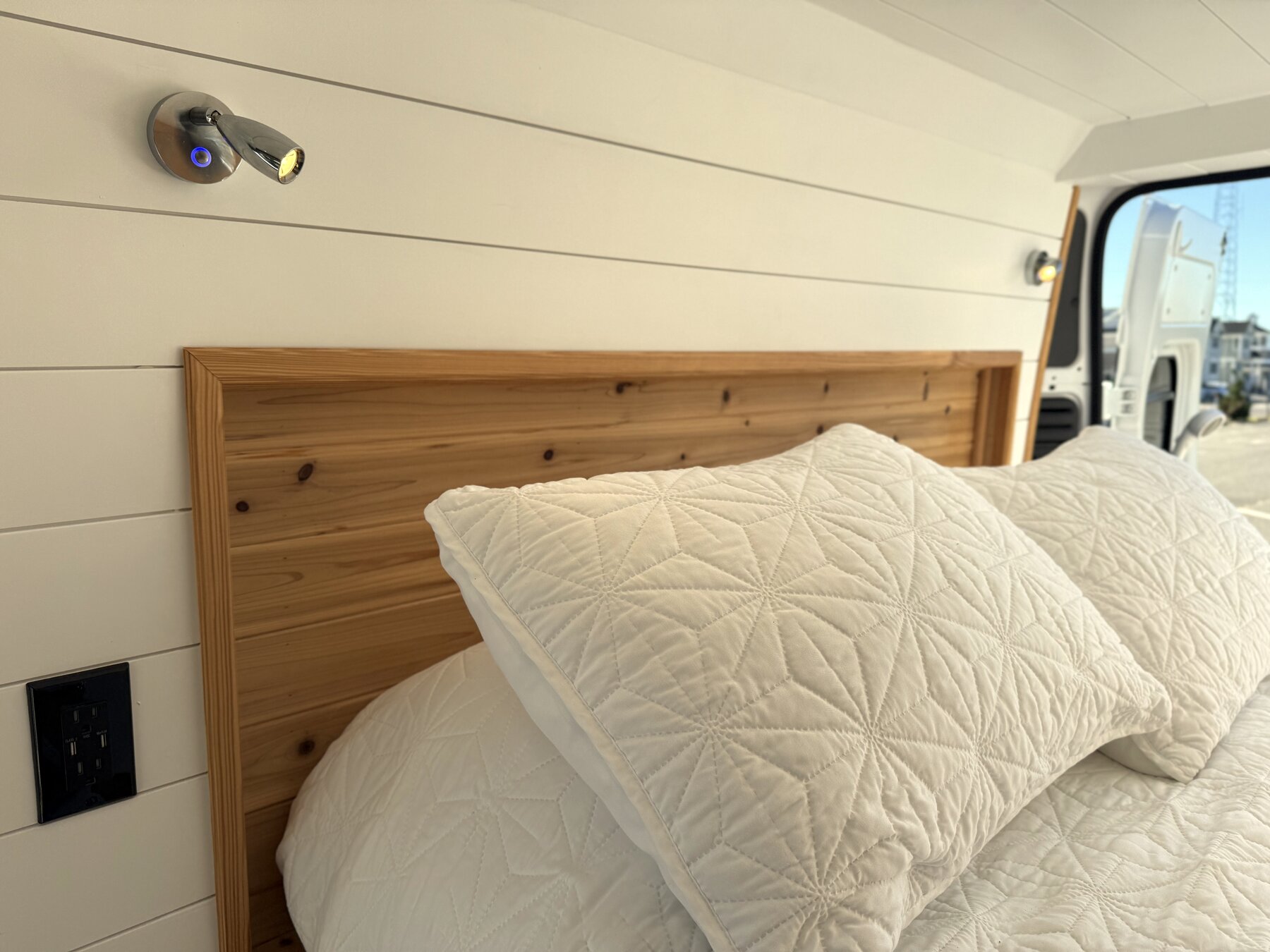 Cedar headboard detail with a reading light and power outlet beside the pillows