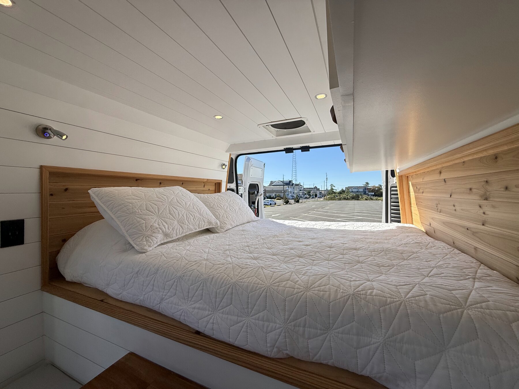 Full-size bed with white bedding and cedar headboard panels, rear doors open behind it