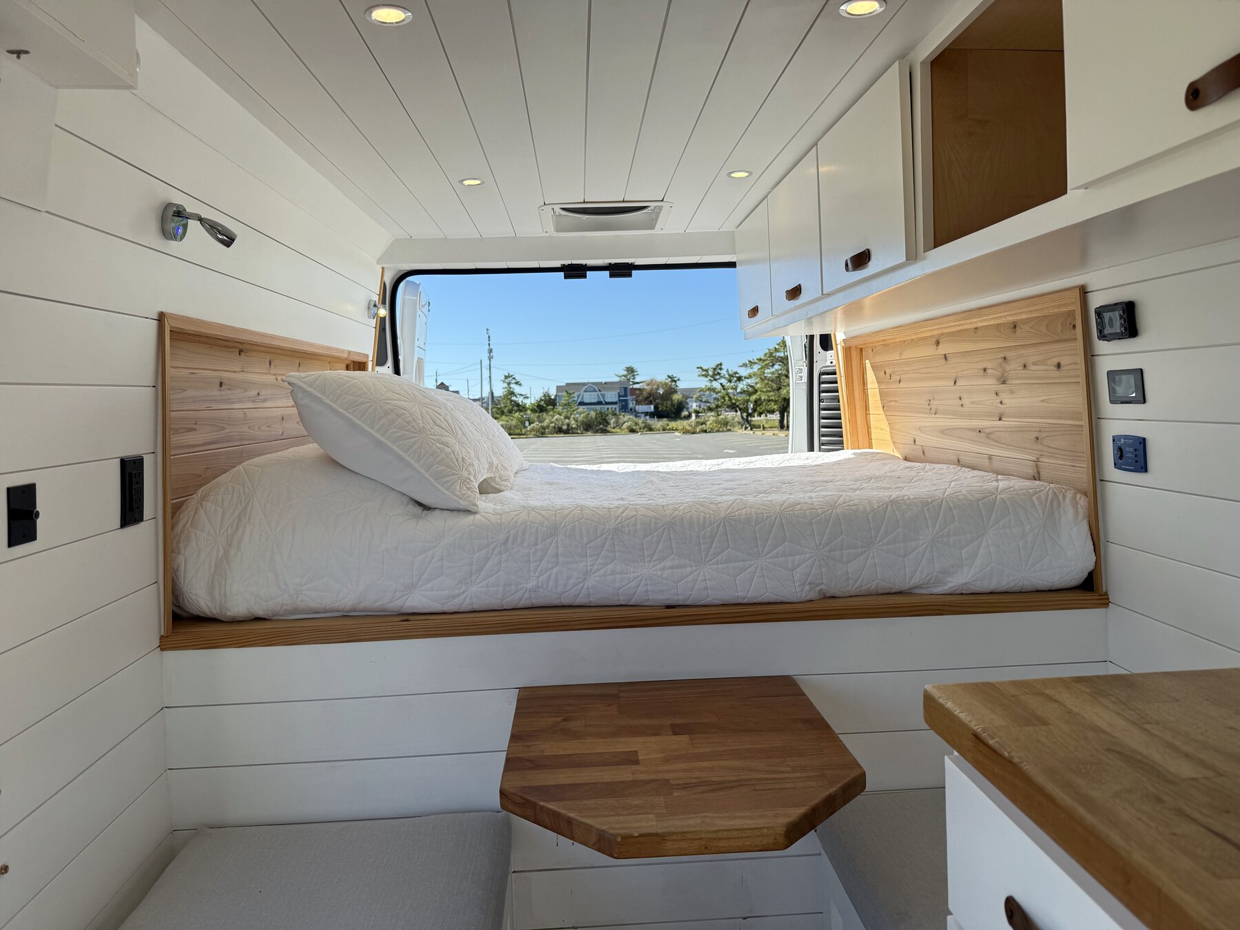 View from the front of the van toward the bed, with the bench seats and wood table between