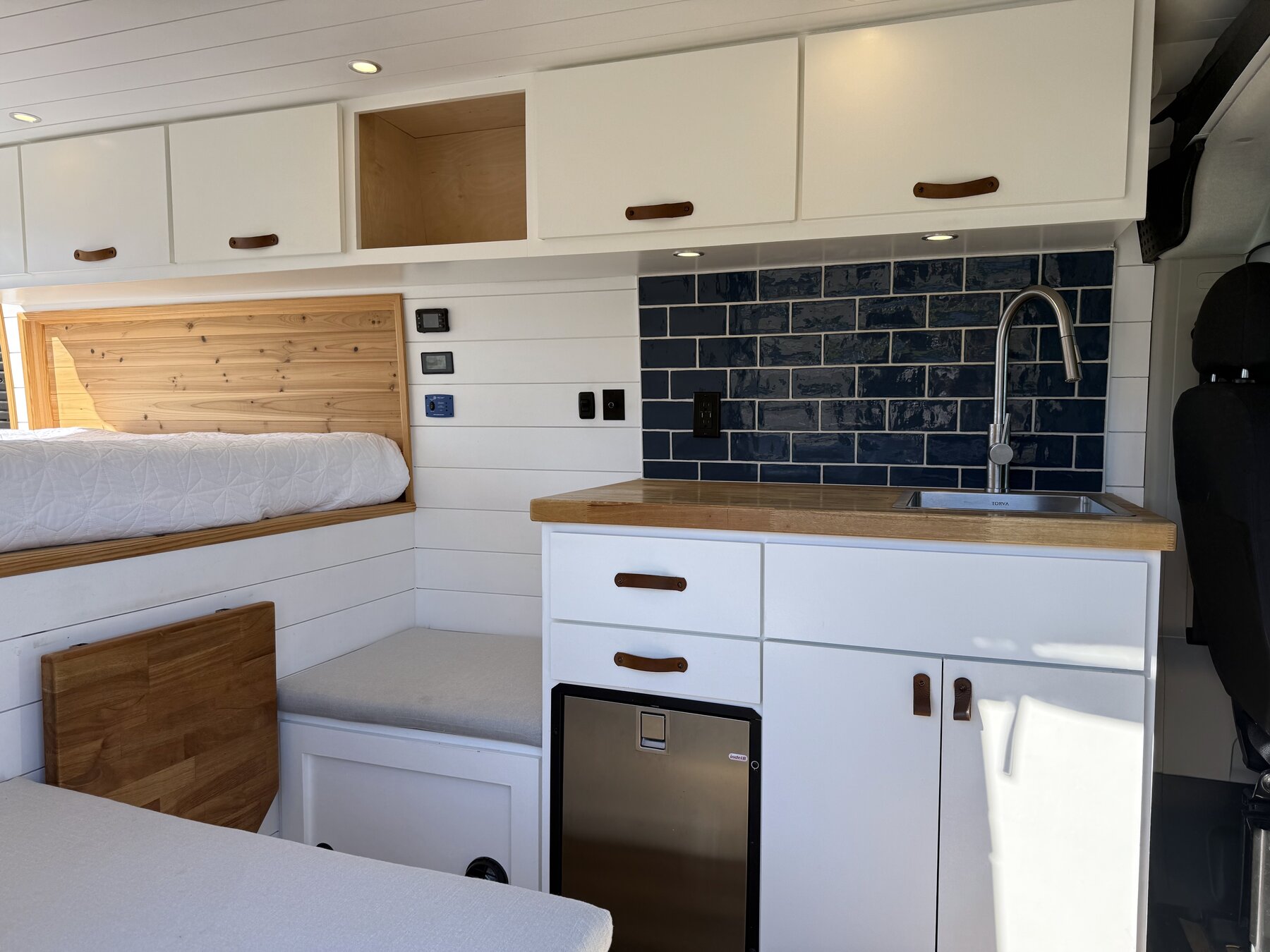 Wide view of the living area: bench seat, white cabinetry, butcher block counter and navy tile backsplash