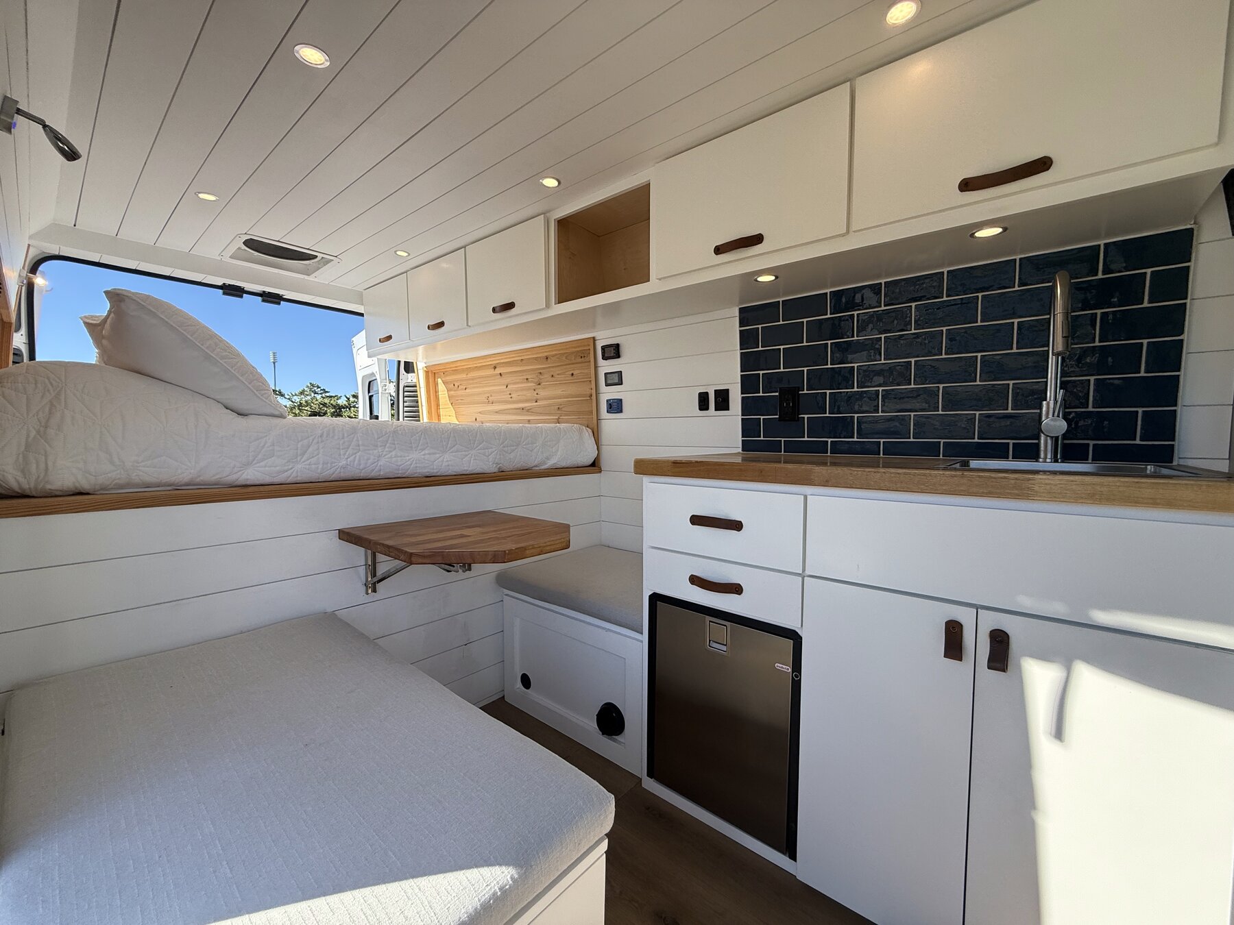 Living area looking toward the rear, with the fold-down table, bench, fridge cabinet and bed beyond