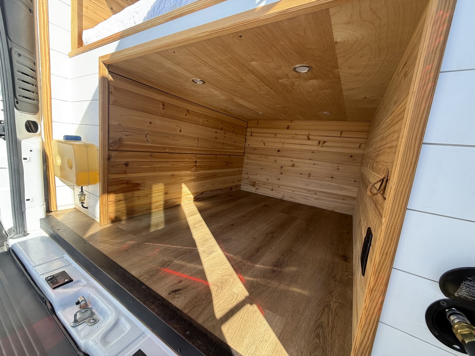 Cedar-lined gear garage under the bed with a wood-look floor and interior light