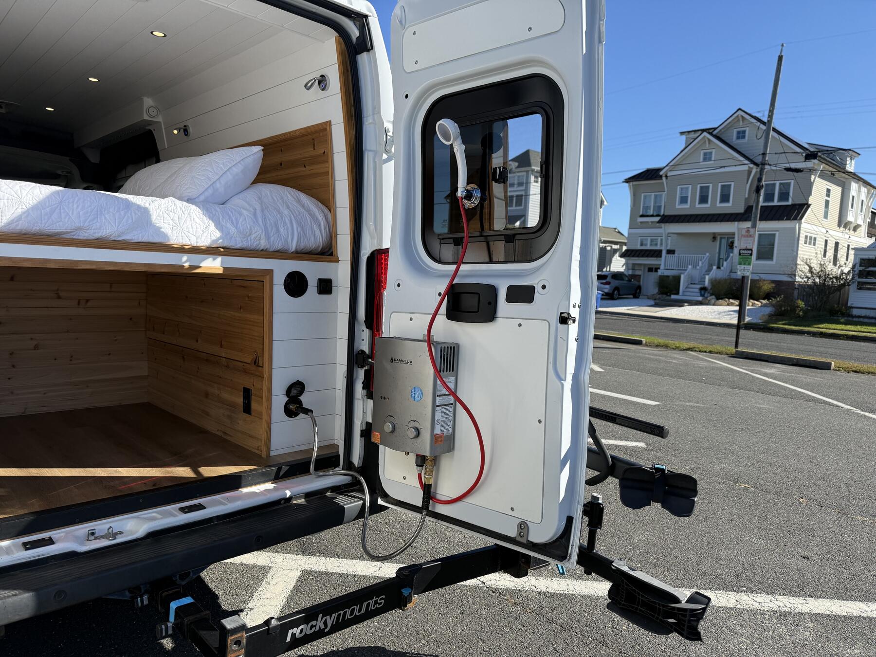 Rear door open with a Camplux water heater and shower hose mounted on it