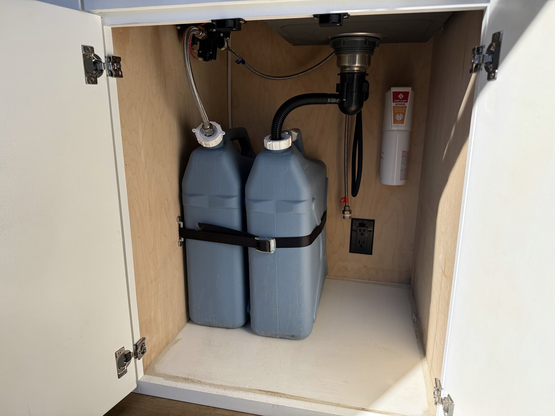 Under-sink cabinet with two water jugs and the sink plumbing