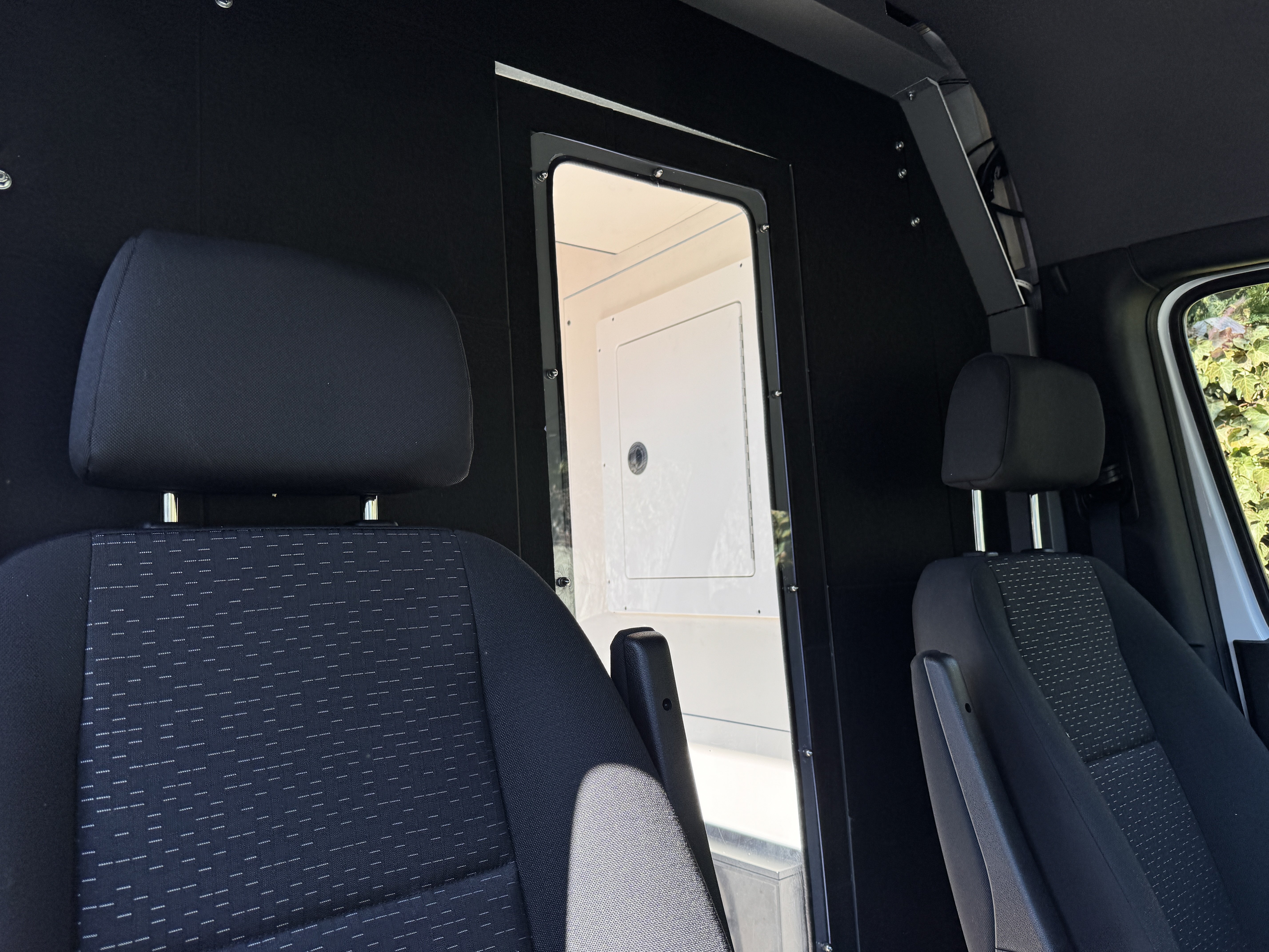 K9 transport Sprinter — handler perspective from cab through partition window into kennel array