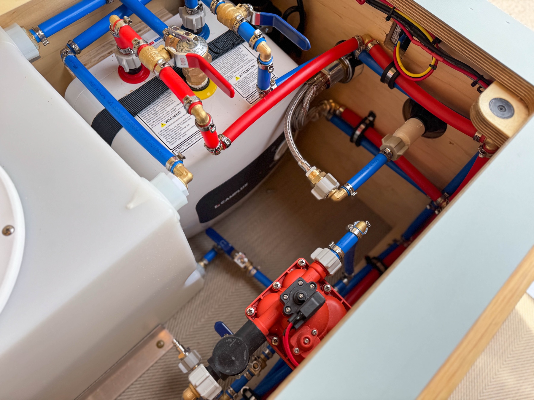Loft van plumbing bay with Camplux water heater, PEX water lines, and marine-grade fittings
