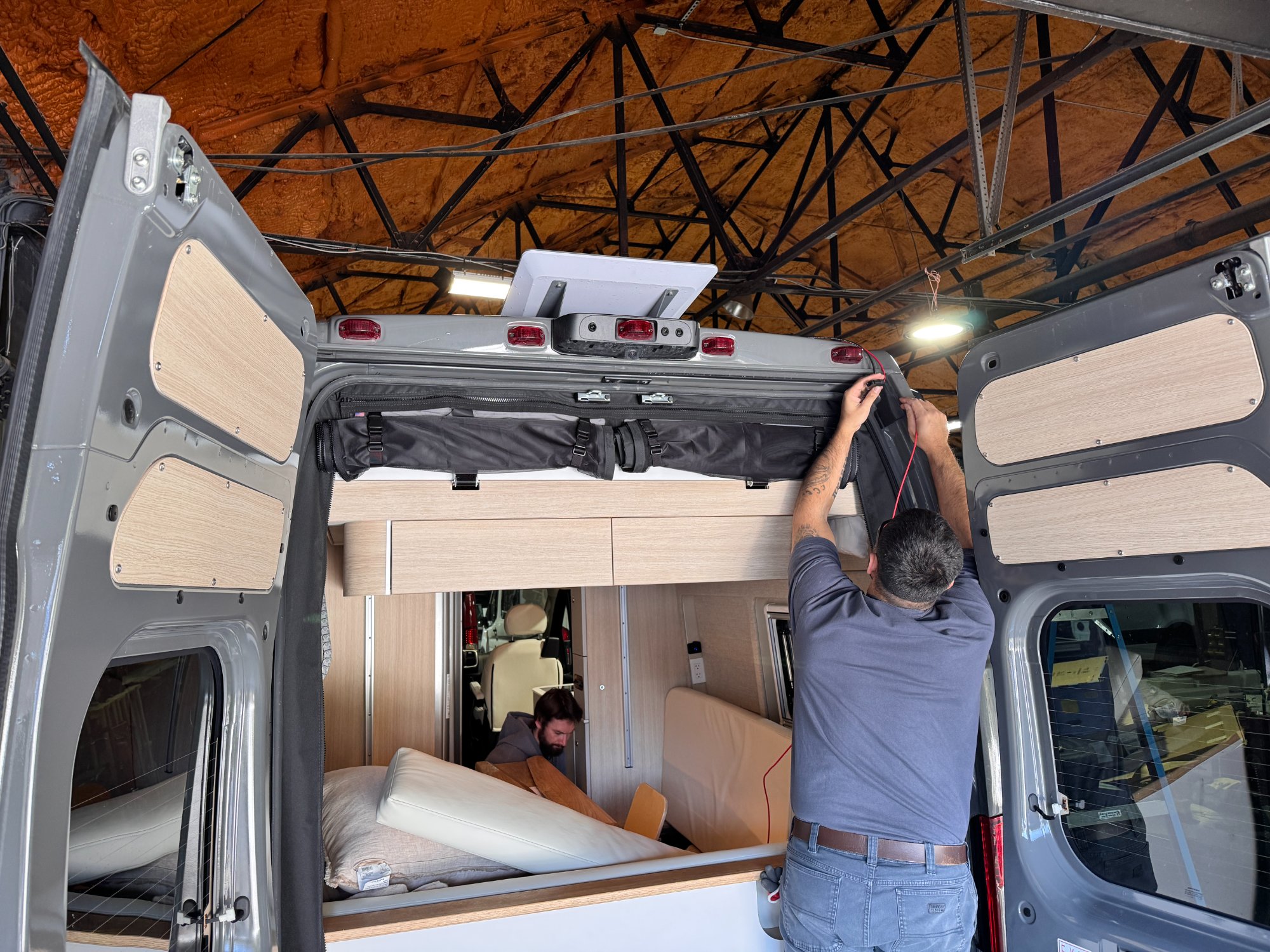 Sequoia + Salt build team — two craftsmen working on a Sprinter conversion in the Manasquan shop, one wiring the rear door and one assembling cabinetry inside