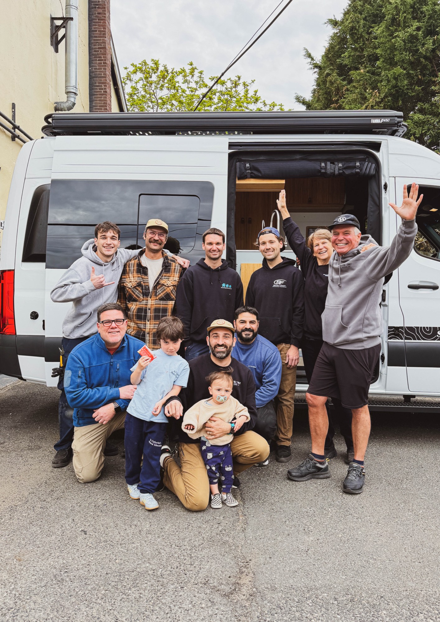 The Sequoia + Salt team with a customer and their family celebrating campervan delivery day in front of a finished Mercedes Sprinter conversion at the Manasquan shop